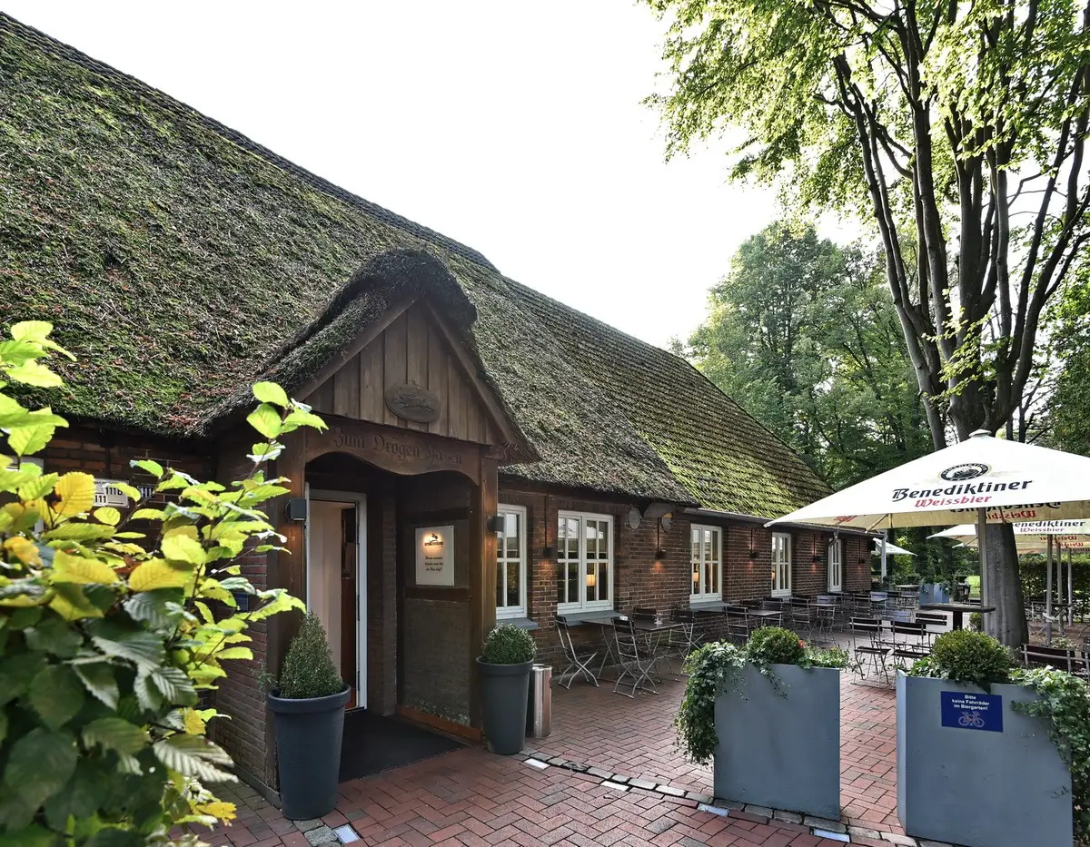 Das Reetdachhaus vom Zum Drögen Hasen mit Terrasse unter alten Bäumen in Oldenburg