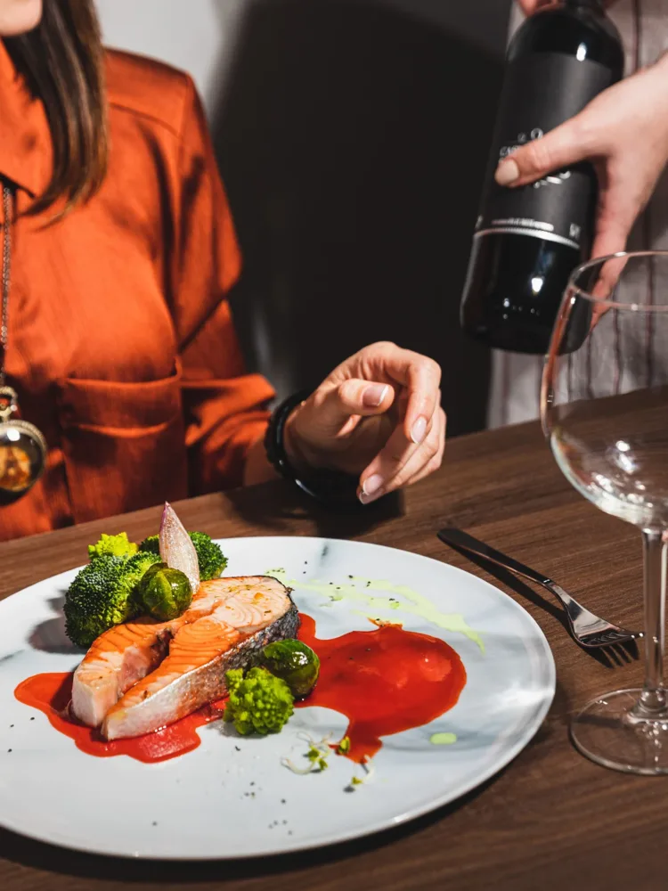 Festlich angerichtetes Lachsfilet mit Brokkoli und Rosenkohl, dazu wird Rotwein eingeschenkt